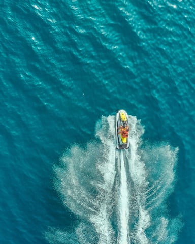 Aerial view of a jet ski cutting through deep blue water with white wake spray