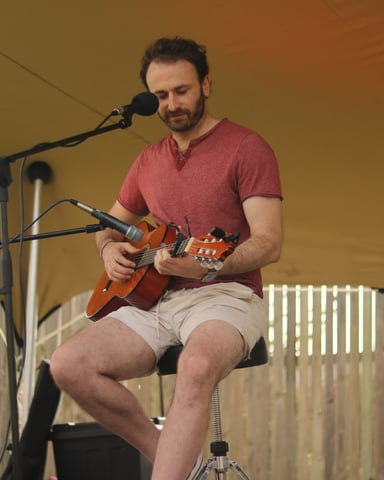 Guitarist performing at an outdoor stage under a tent
