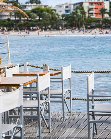 Outdoor waterfront cafe tables with white chairs and turquoise water