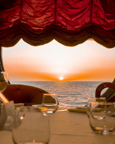Sunset dining table with wine glasses framed through a porthole window