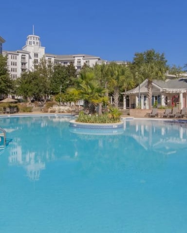 Large resort pool with turquoise water, palm trees, white buildings with cupolas, and lounge chairs under clear blue sky