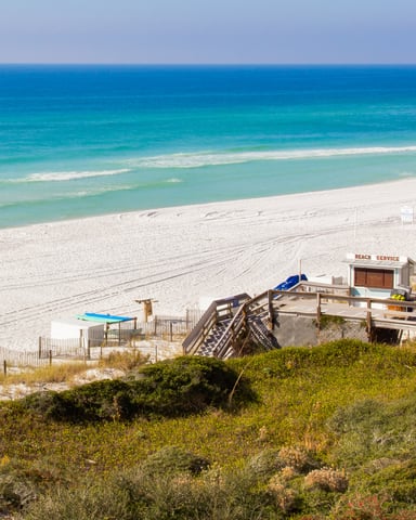 Sandy beach with turquoise water, wooden boardwalk, beach service station, and yellow flag