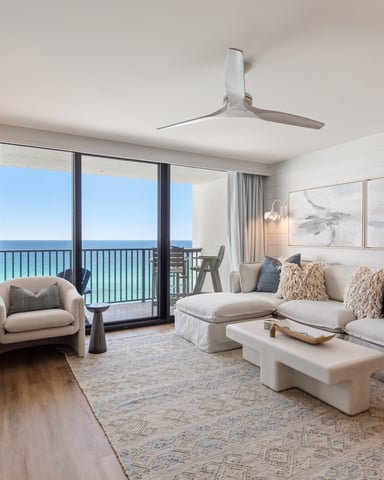 Spacious beige living room with ocean view balcony, cream sectional sofa, armchairs, and modern ceiling fan