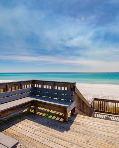 Wooden beach deck with built-in seating overlooking white sand and turquoise ocean under blue sky
