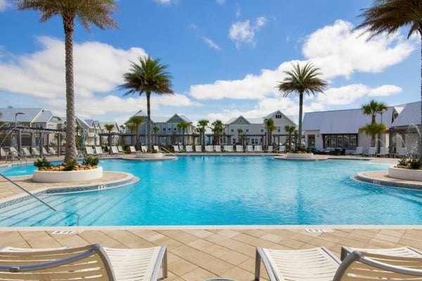 Resort pool with palm trees, lounge chairs, and colorful residential buildings under blue sky