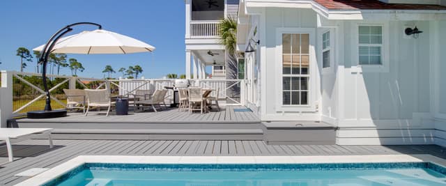 Modern white beach house with pool, wooden deck, lounge chairs, and cantilever umbrella overlooking palm trees