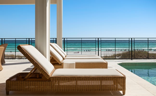 Wicker lounge chairs beside a private pool with the Gulf of Mexico visible beyond the railing