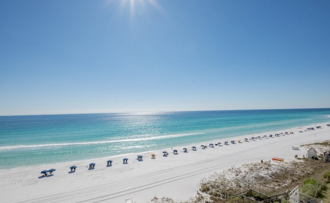 Oceanfront deck with lounge chairs overlooking turquoise water, sandy beach, and coastal vegetation