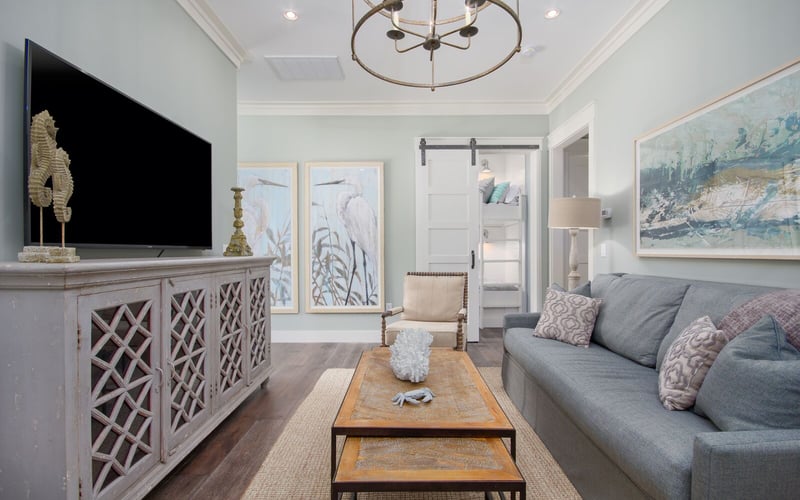 Bright living room with gray sofa, TV on decorative cabinet, coastal artwork, and round ceiling fixture