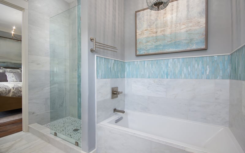 Modern bathroom with white marble tiles, glass-enclosed shower, soaking tub, and coastal artwork on walls