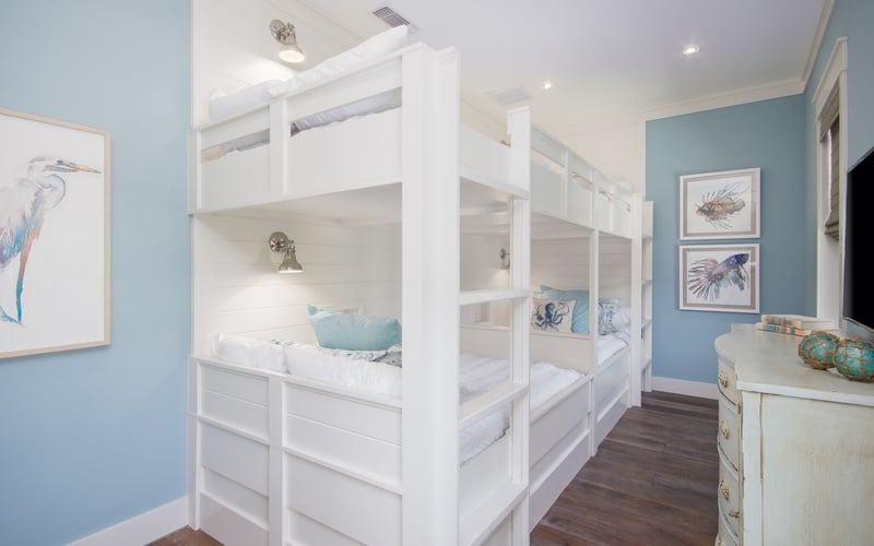 Children's bedroom with white built-in bunk beds, blue walls, fish artwork, and wooden flooring